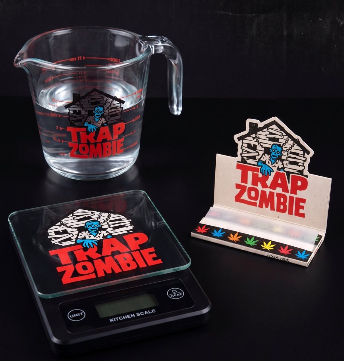 Trap Zombie glass measuring cup, digital kitchen scale and rolling papers on a black table